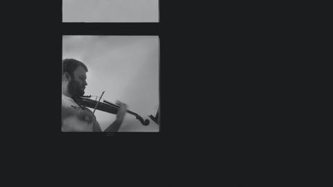 Ein Mann spielt hinter einem Fenster Geige.