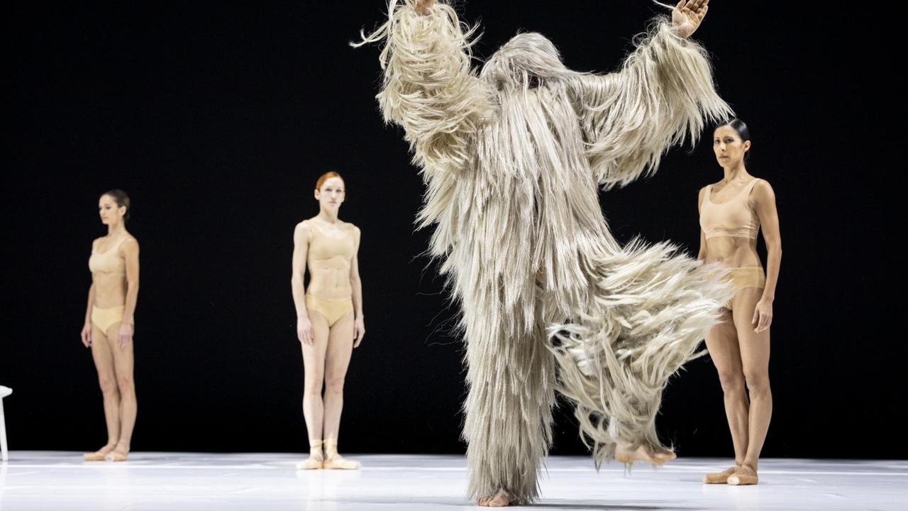Im Szenenbild der Tanzperformance "LIB" stehen drei Tänzerinnen und ein Darsteller in Fellkostüm auf der Bühne. Im Szenenbild der Tanzperformance "LIB" stehen drei Tänzerinnen und ein Darsteller in Fellkostüm auf der Bühne.