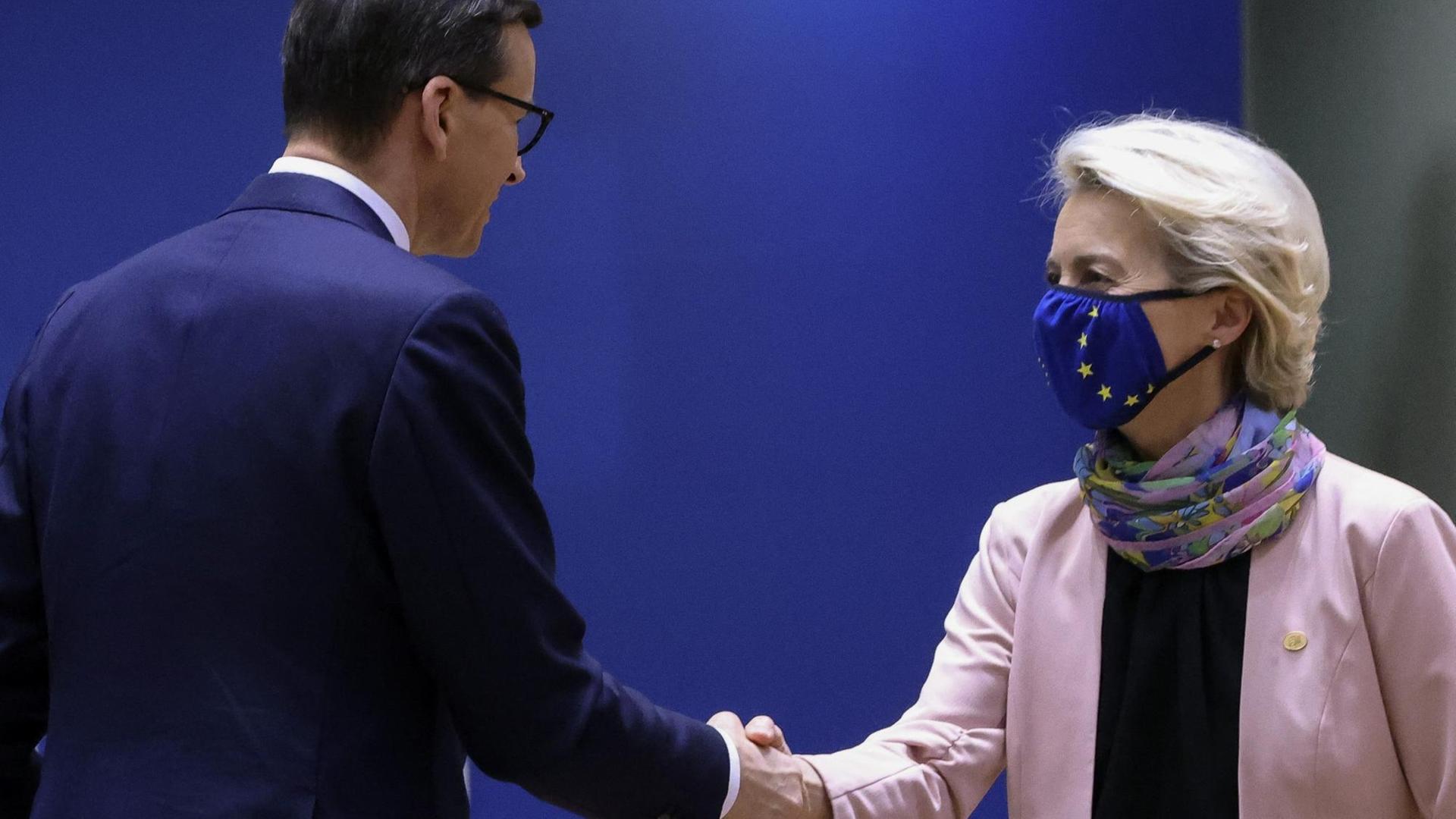 Mateusz Morawiecki und Ursula von der Leyen schütteln einander die Hände. Sie trägt dabei eine Maske mit dem Logo der EU. Mateusz Morawiecki und Ursula von der Leyen schütteln einander die Hände. Sie trägt dabei eine Maske mit dem Logo der EU.