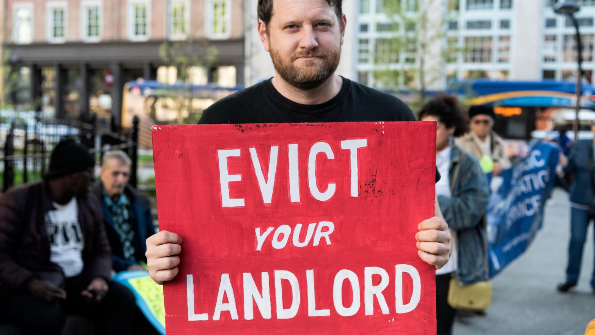 Ein Mann hält ein Schild auf dem steht "Evict you Landlord". Ein Mann hält ein Schild auf dem steht "Evict you Landlord".