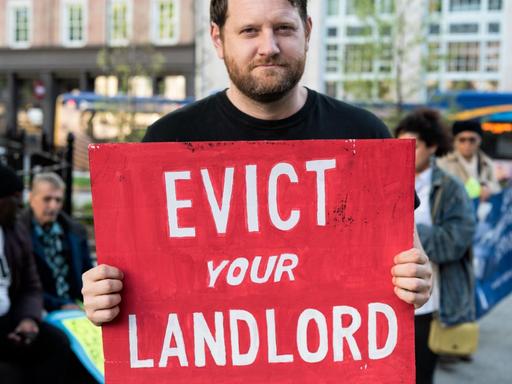Ein Mann hält ein Schild auf dem steht "Evict you Landlord".
