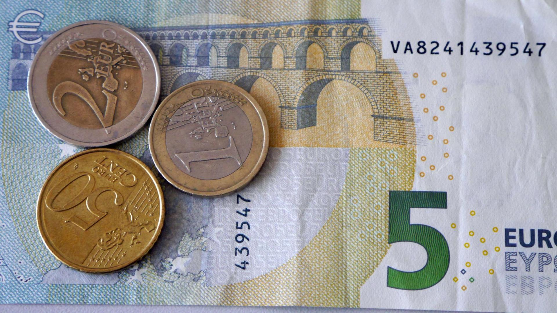 Ein Fünf-Euro-Schein liegt mit einem Ein- und Zwei-Euro und einem 50-Cent-Stück auf einem Stapel. Ein Fünf-Euro-Schein liegt mit einem Ein- und Zwei-Euro und einem 50-Cent-Stück auf einem Stapel.