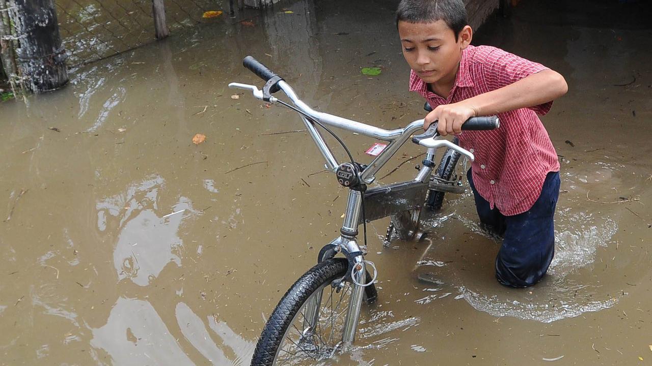 Ein Junge im rotkarierten Hemd kämpft sich mit seinem Fahrrad durch eine überschwemmte Straße in Honduras. . Ein Junge im rotkarierten Hemd kämpft sich mit seinem Fahrrad durch eine überschwemmte Straße in Honduras. .