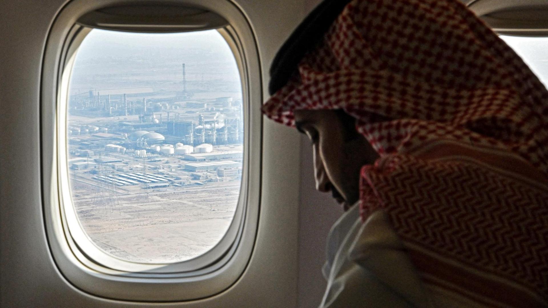 Ein saudischer Mann schaut durch ein Flugzeugfenster, durch das eine Ölraffinerie zu sehen ist.
