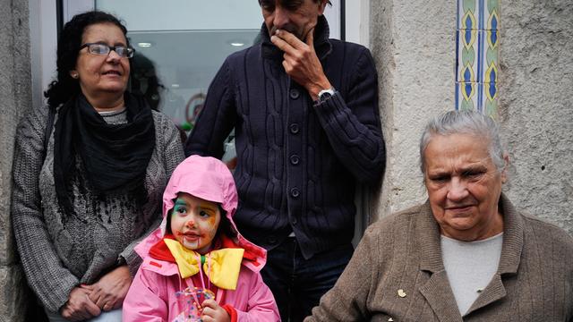 Ein als Clown verkleidetes Kind zwischen Erwachsenen beim Karneval in Sesimbra, Portugal.