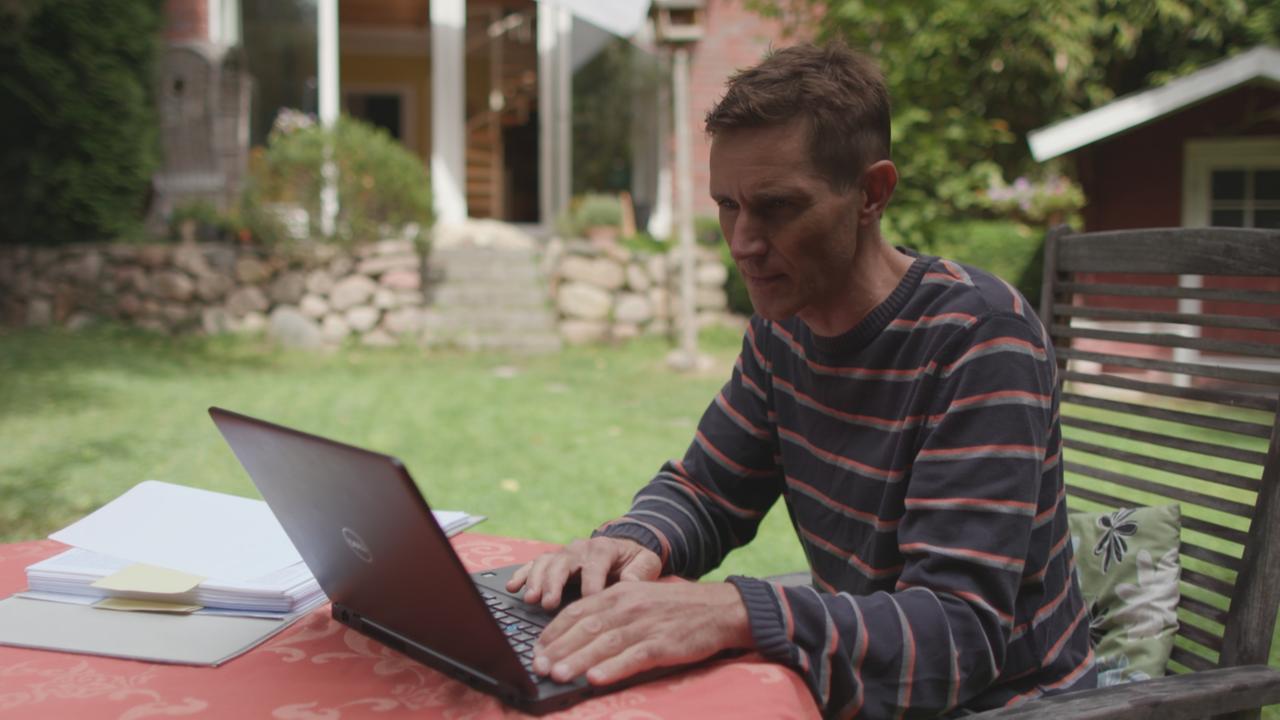 Ein Mann sitzt in einem Garten an einem Laptop.
