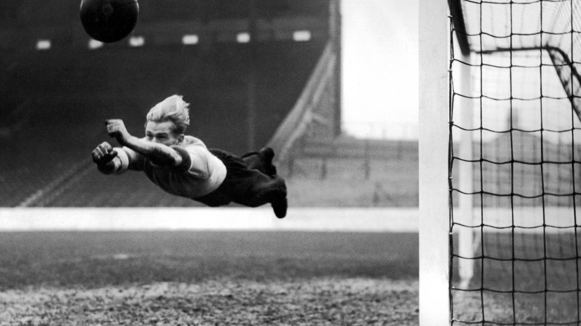 Torhüter Bert Trautmann springt einem Ball vor dem Tor hinterher. Auf dem Schwarz-Weiß-Foto aus dem Jahr 1952 liegt er waagerecht in der Luft, der Ball ist weit vor ihm.