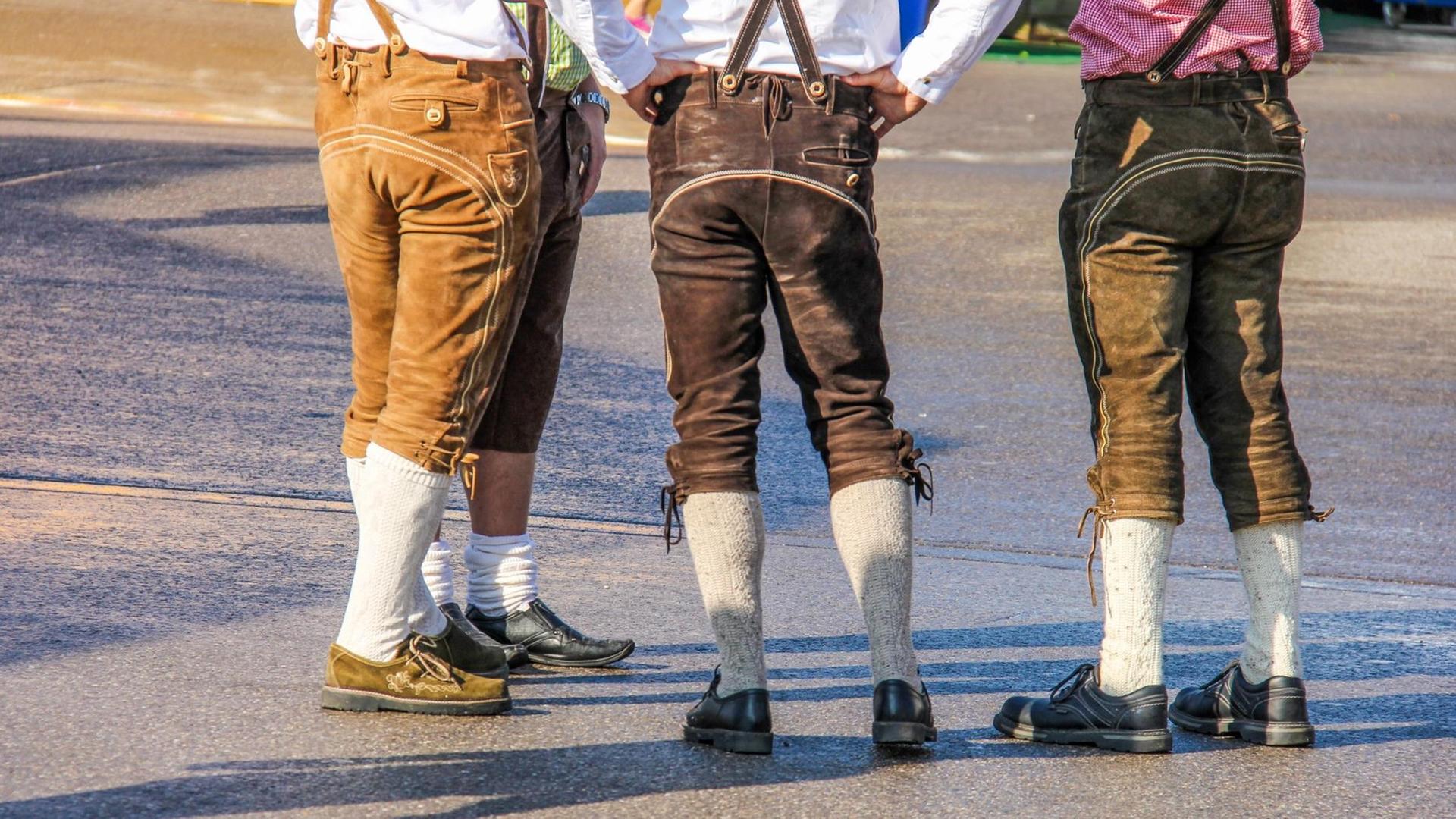 Rückansicht auf Beine und Po dreier junger Männer in folkloristischer Lederhosen-Tracht auf dem Münchner Oktoberfest.