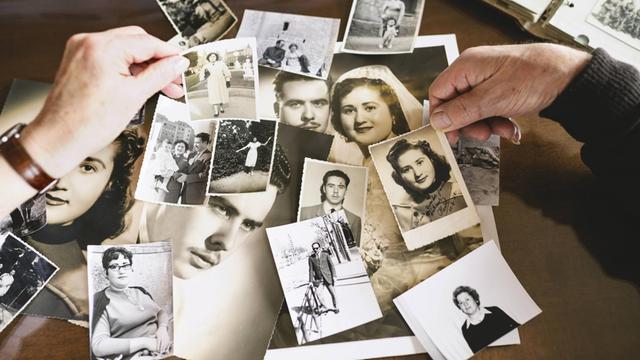 Das Bild zeigt einen Tisch voller alter schwarz-weiss Fotos sowie die Hände von Senioren, die Bilder auswählen.