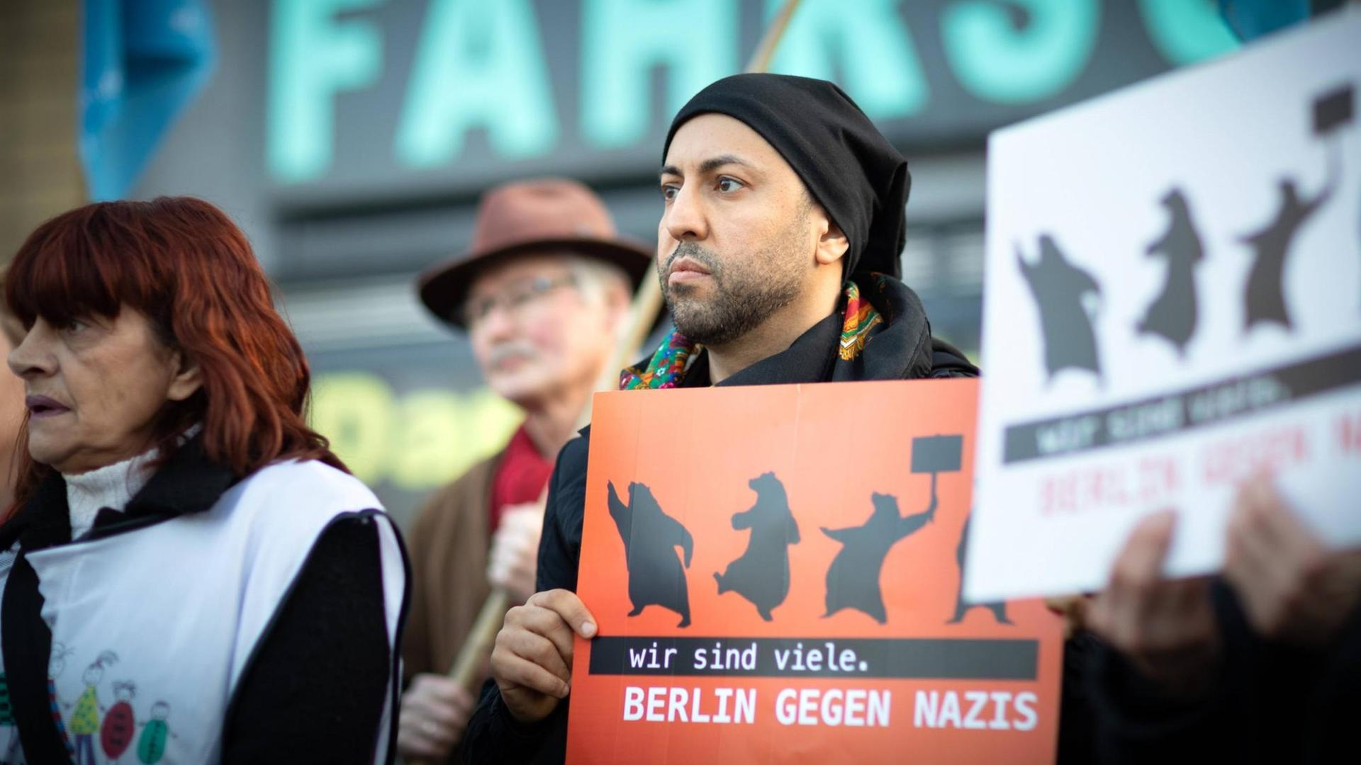 Ferat Kocak steht in einer Kundgebung in Berlin-Neukölln mit einem Schild auf dem steht: Wir sind mehr. Berlin gegen Nazis. Ferat Kocak steht in einer Kundgebung in Berlin-Neukölln mit einem Schild auf dem steht: Wir sind mehr. Berlin gegen Nazis.