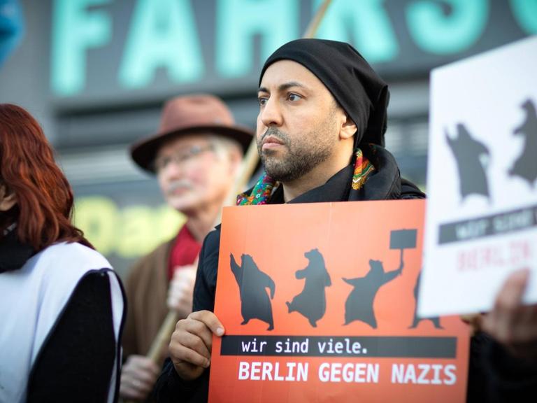 Ferat Kocak steht in einer Kundgebung in Berlin-Neukölln mit einem Schild auf dem steht: Wir sind mehr. Berlin gegen Nazis.