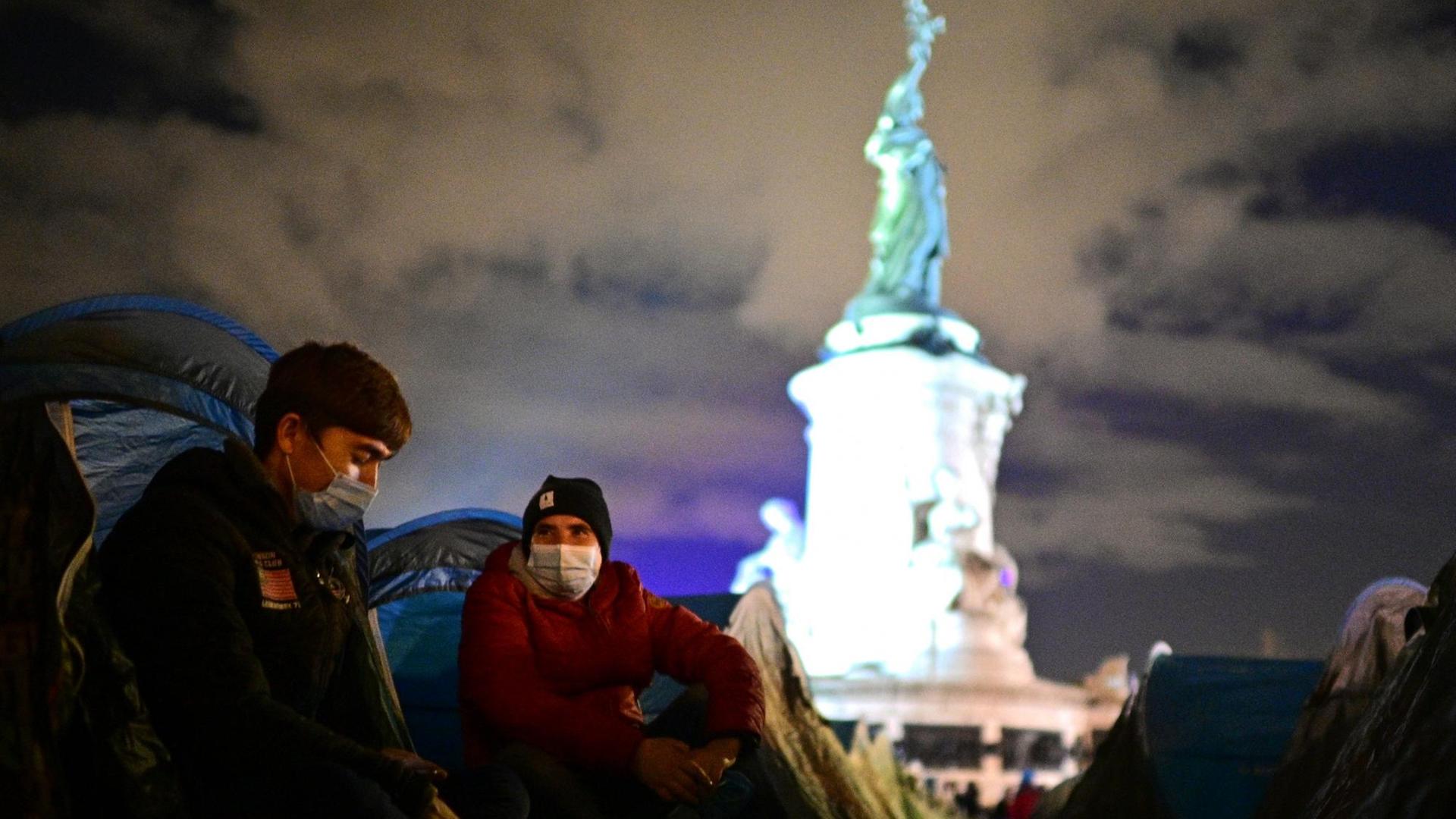 Zwei Männer sitzen vor ihren Zelten am 23. November 2020 auf demPariser Place de la République, im Hintergrund die Marianne – die Symbolfigur der Republik. Zwei Männer sitzen vor ihren Zelten am 23. November 2020 auf demPariser Place de la République, im Hintergrund die Marianne – die Symbolfigur der Republik.