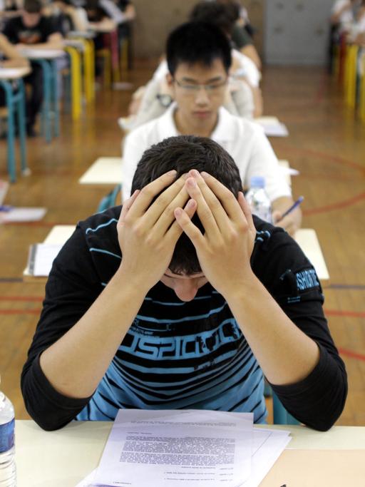 Schüler an Schreibtischen beim Pisa-Test. Der Schüler vorne im Bild hat seine Hände über dem Kopf gefaltet.