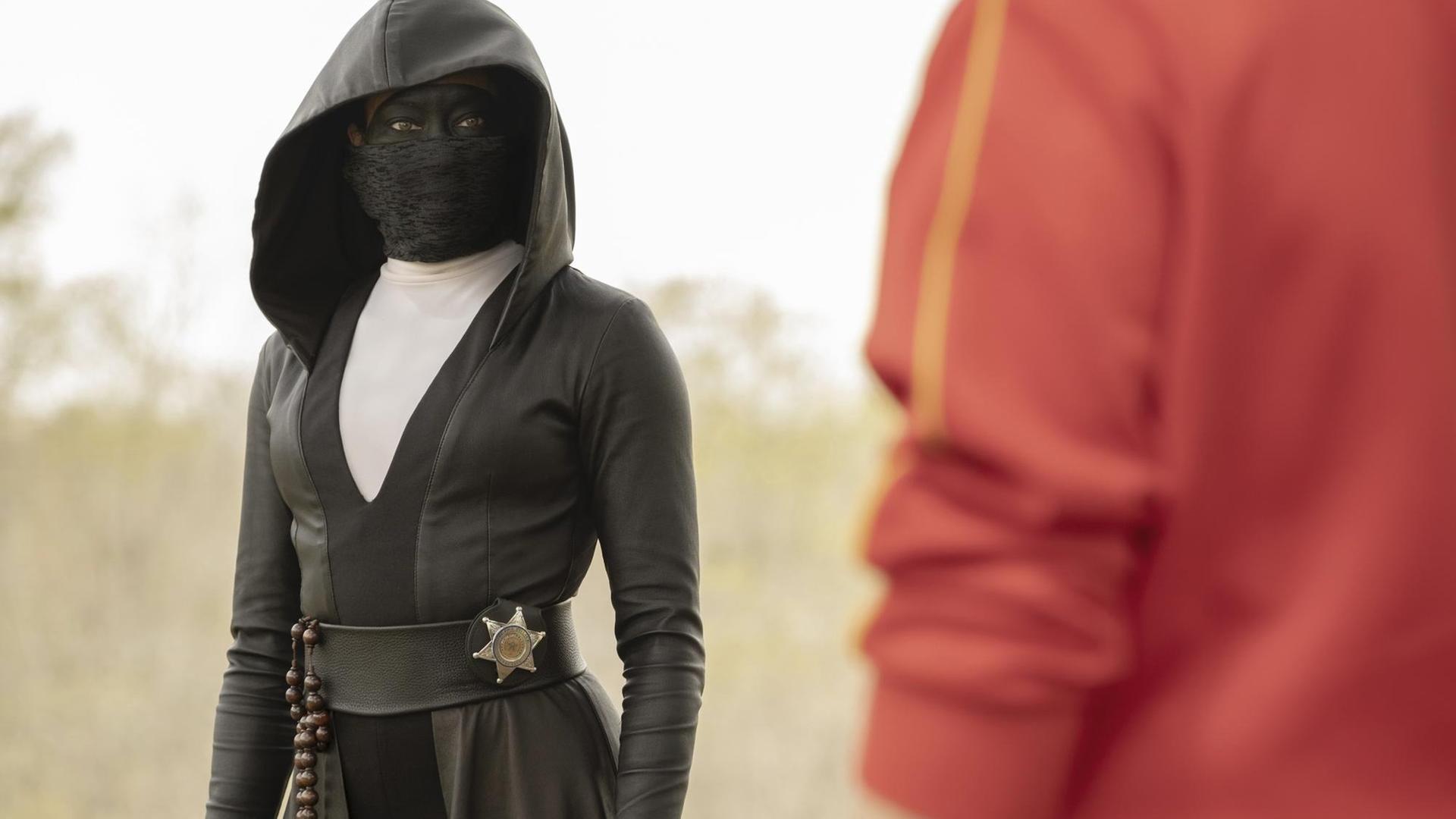 Eine schwarz verhüllte Frau mit Maske trägt einen Sheriffstern an der Hüfte. Eine schwarz verhüllte Frau mit Maske trägt einen Sheriffstern an der Hüfte.