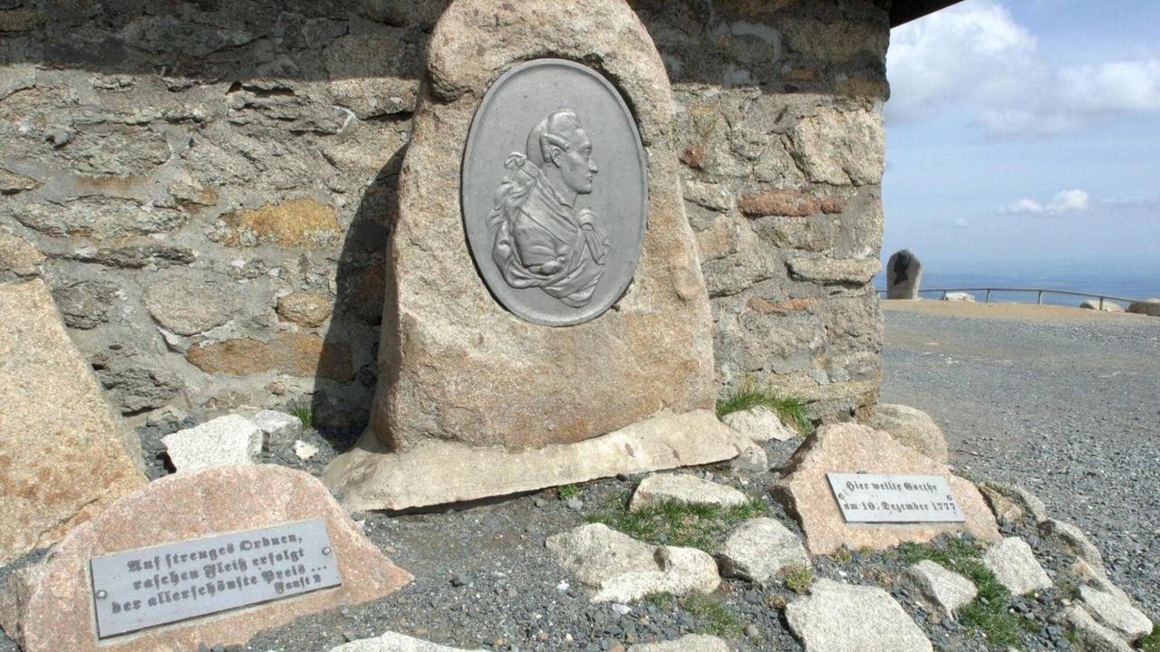 Ein außerhalb einer Berghütte stehender Gedenkstein mit dem aufgeprägten Konterfei Goethes.