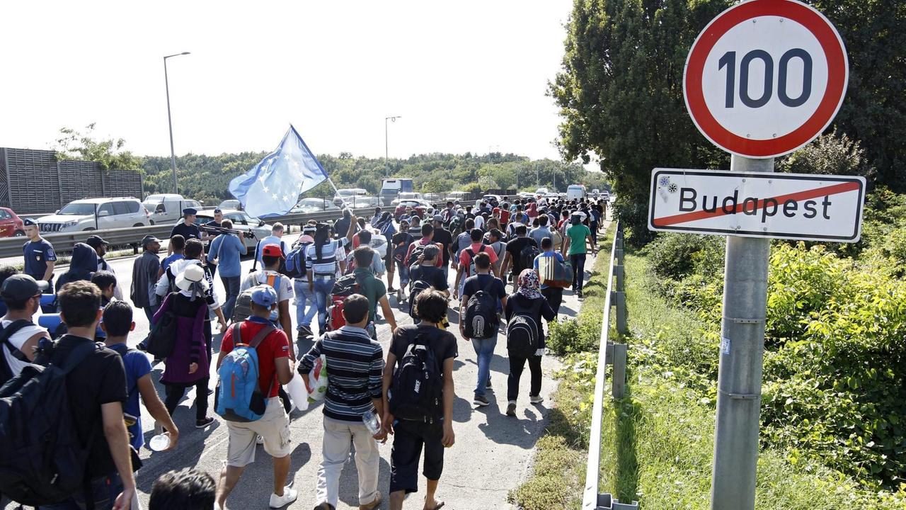 Flüchtlinge laufen auf einer Straße und passieren das Ortsausgangsschild von Budapest. Flüchtlinge laufen auf einer Straße und passieren das Ortsausgangsschild von Budapest.