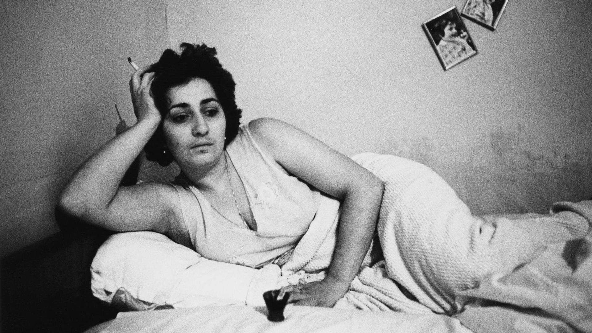 Eine Frau liegt auf einem Bett, ihre Zigarette in der Hand. Ohne Titel, aus der Serie "Georgien", 1982, von Helga Paris. Eine Frau liegt auf einem Bett, ihre Zigarette in der Hand. Ohne Titel, aus der Serie "Georgien", 1982, von Helga Paris.