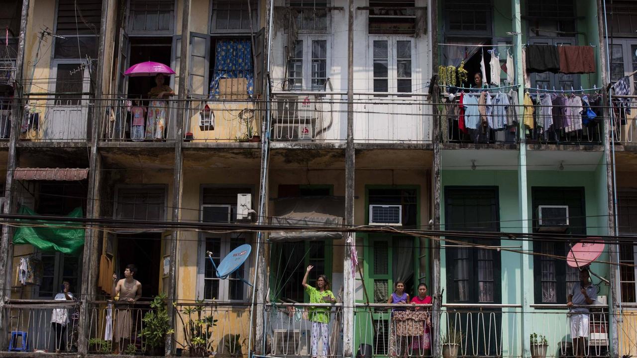 Bewohner eines Wohnblocks in Yangon stehen auf ihren Balkons und schauen auf die Straße.
