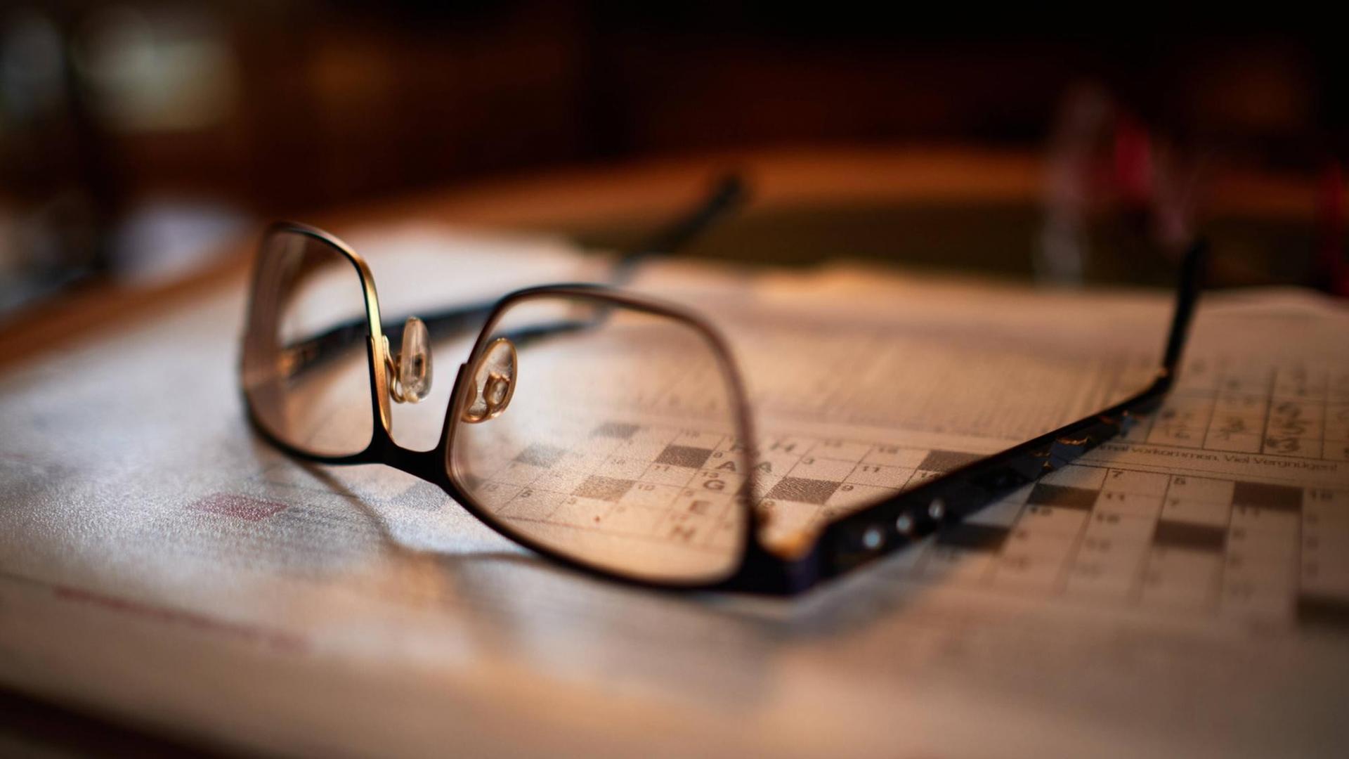 Lesebrille liegt auf Tisch mit Kreuzworträtsel Lesebrille liegt auf Tisch mit Kreuzworträtsel