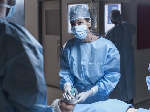 Ein Operationsteam im Krankenhaus. Eine Frau auf der Liege bekommt ein Beatmungsgerät aufgesetzt.