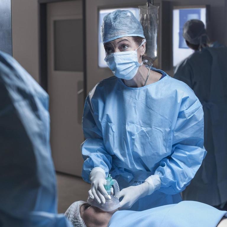 Ein Operationsteam im Krankenhaus. Eine Frau auf der Liege bekommt ein Beatmungsgerät aufgesetzt. 