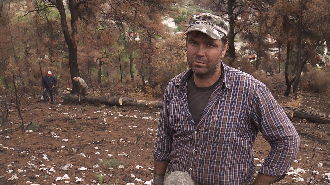 Ein Mann mit ernstem Blick, kariertem Hemd und Käppi steht in einer kahlen Landschaft zwischen herumliegenden dicken Baumstämmen. Ein Mann mit ernstem Blick, kariertem Hemd und Käppi steht in einer kahlen Landschaft zwischen herumliegenden dicken Baumstämmen.