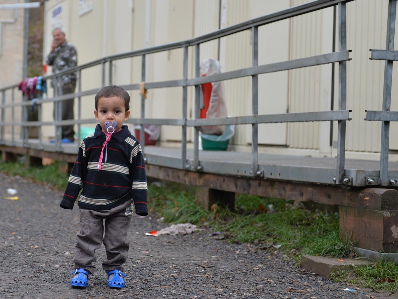 Ein Kleinkind steht am 21.11.2013 in Eisenberg (Thüringen) auf dem Gelände der Erstaufnahmestelle für Flüchtlinge und Asylbewerber vor Wohncontainern. Die Suche nach einer neuen Erstaufnahmestelle für Flüchtlinge in Thüringen gestaltet sich weiterhin schwierig. Es sei noch keine Entscheidung gefallen, sagte ein Sprecher des Innenministeriums der Nachrichtenagentur dpa in Erfurt. Ein Kleinkind steht am 21.11.2013 in Eisenberg (Thüringen) auf dem Gelände der Erstaufnahmestelle für Flüchtlinge und Asylbewerber vor Wohncontainern. Die Suche nach einer neuen Erstaufnahmestelle für Flüchtlinge in Thüringen gestaltet sich weiterhin schwierig. Es sei noch keine Entscheidung gefallen, sagte ein Sprecher des Innenministeriums der Nachrichtenagentur dpa in Erfurt.