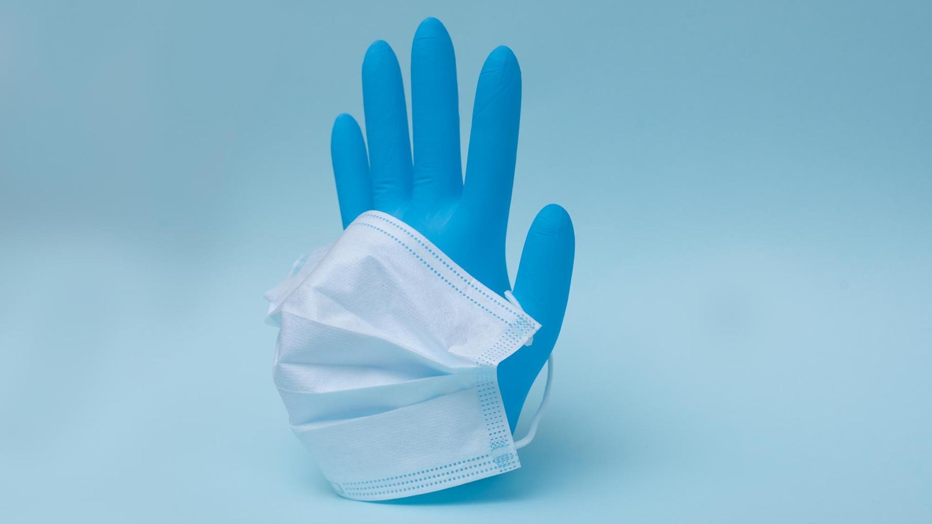 Vor blauem Hintergrund ist ein blauer Handschuh mit Atemmmaske aufgestellt.