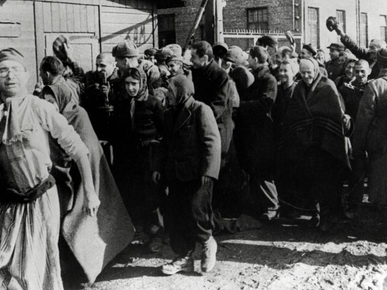 Überlebende des Konzentrationslagers Auschwitz verlassen das Lager und machen dabei Siegesgesten.