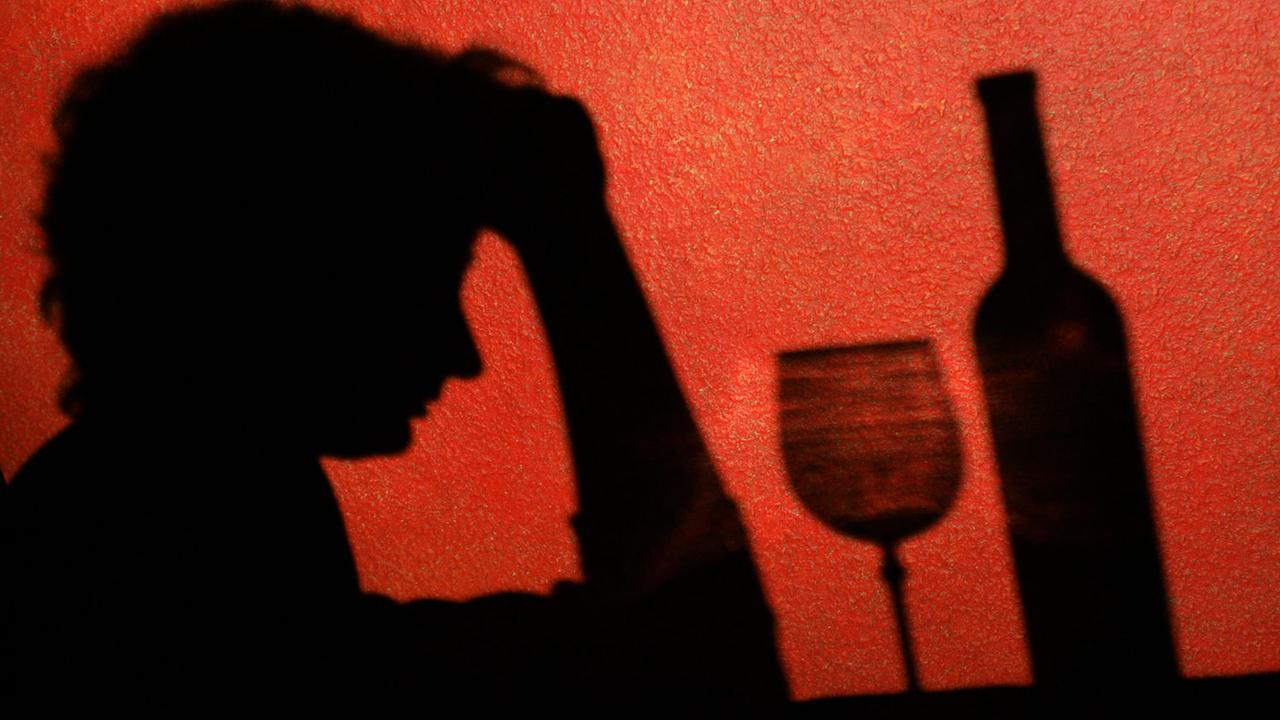 Der Schatten einer Frau, die nachdenklich vor einem Glas Wein sitzt,