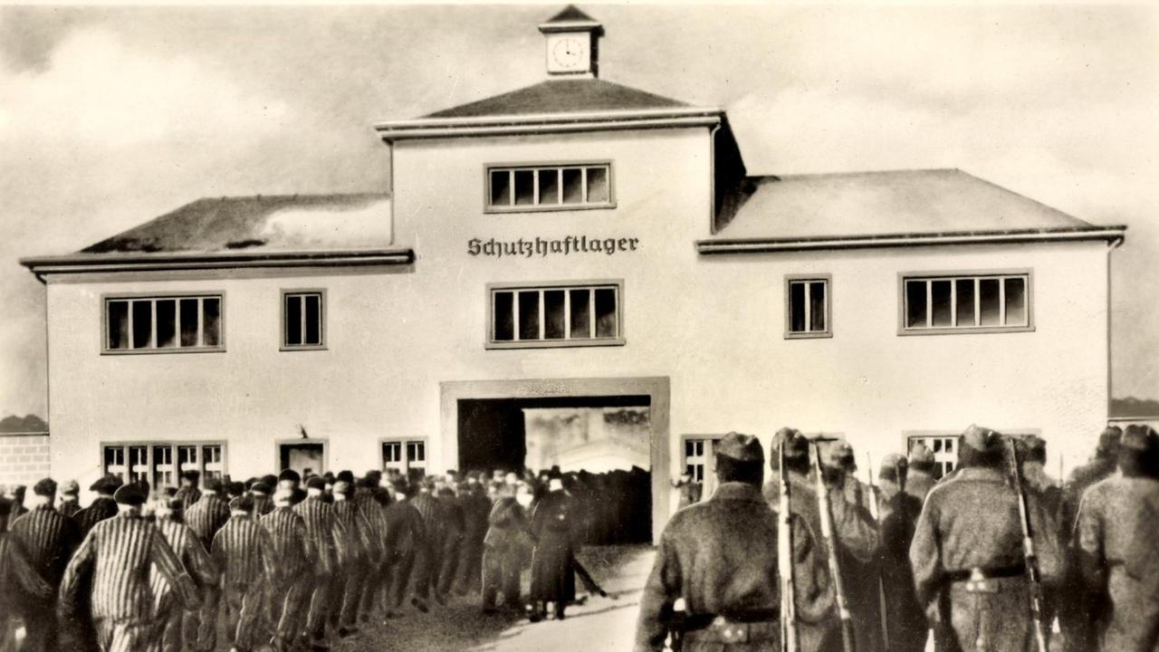 Häftlinge und Wärter stehen vor dem Eingang zum KZ Sachsenhausen. Über dem Tor der Schriftzug: Schutzhaftlager. Häftlinge und Wärter stehen vor dem Eingang zum KZ Sachsenhausen. Über dem Tor der Schriftzug: Schutzhaftlager.