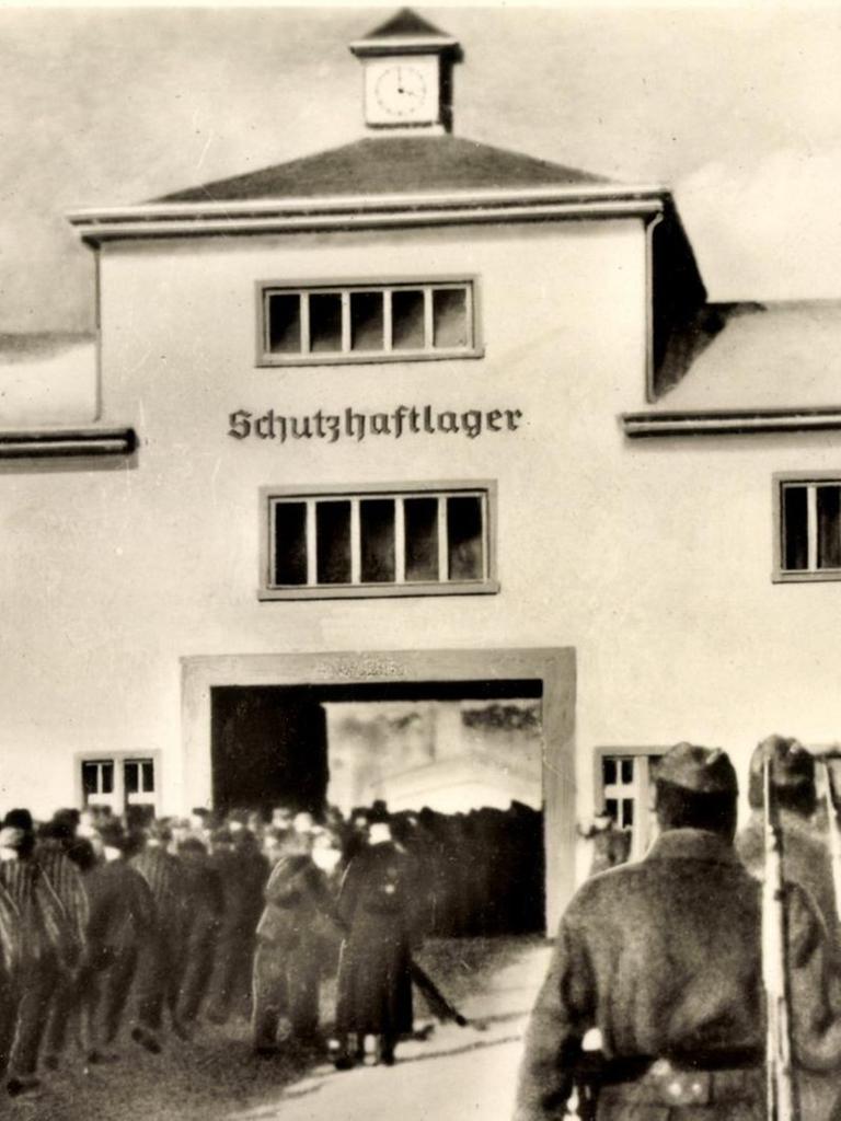 Häftlinge und Wärter stehen vor dem Eingang zum KZ Sachsenhausen. Über dem Tor der Schriftzug: Schutzhaftlager.