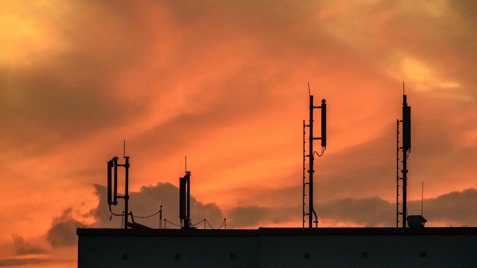 Mobilfunk-Antennen auf einem Dach während des Sonnenuntergangs Mobilfunk-Antennen auf einem Dach während des Sonnenuntergangs
