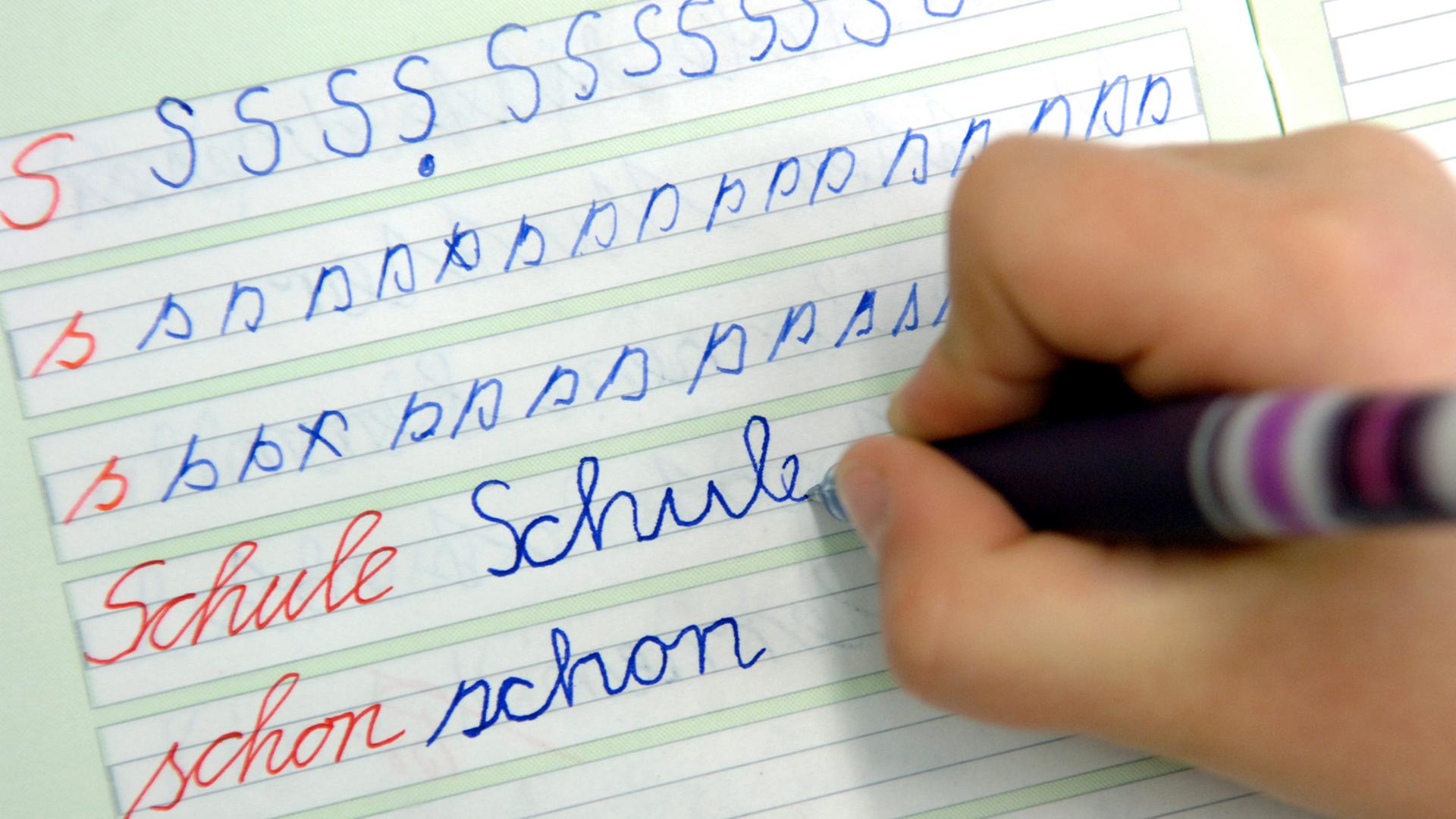Ein Mädchen schreibt im Unterricht das Wort "Schule" in ihr Heft.