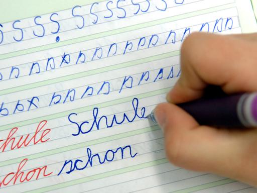 Ein Mädchen schreibt im Unterricht das Wort "Schule" in ihr Heft.