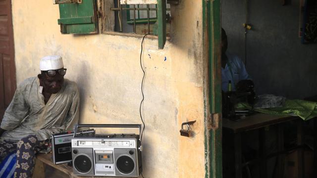 Ein älterer Mann aus dem Togo sitzt vor seinem Haus und hört Radio