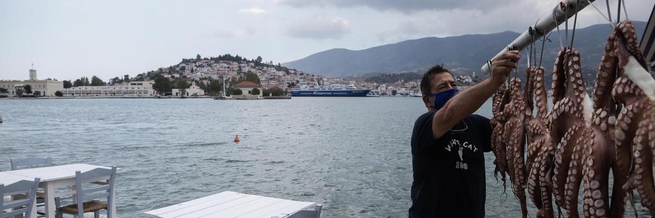 Ein Mann hängt Oktopusse auf der kleinen Urlaubsinsel Poros auf. Dort gelten wieder strenge Coronavorschriften. Ein Mann hängt Oktopusse auf der kleinen Urlaubsinsel Poros auf. Dort gelten wieder strenge Coronavorschriften.