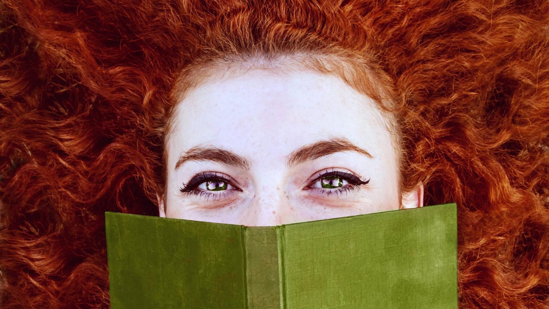 Junge rothaarige Frau bedeckt ihr Gesicht mit einem Buch. Junge rothaarige Frau bedeckt ihr Gesicht mit einem Buch.