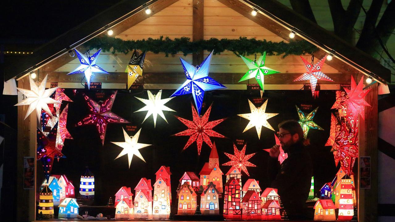 Beleuchtete Papiersterne und Papierhäuser an einem Stand auf dem Weihnachtsmarkt. Beleuchtete Papiersterne und Papierhäuser an einem Stand auf dem Weihnachtsmarkt.