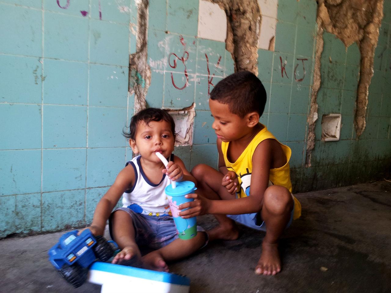Ein Junge reicht einem anderen Kind eine Trinkflasche. 