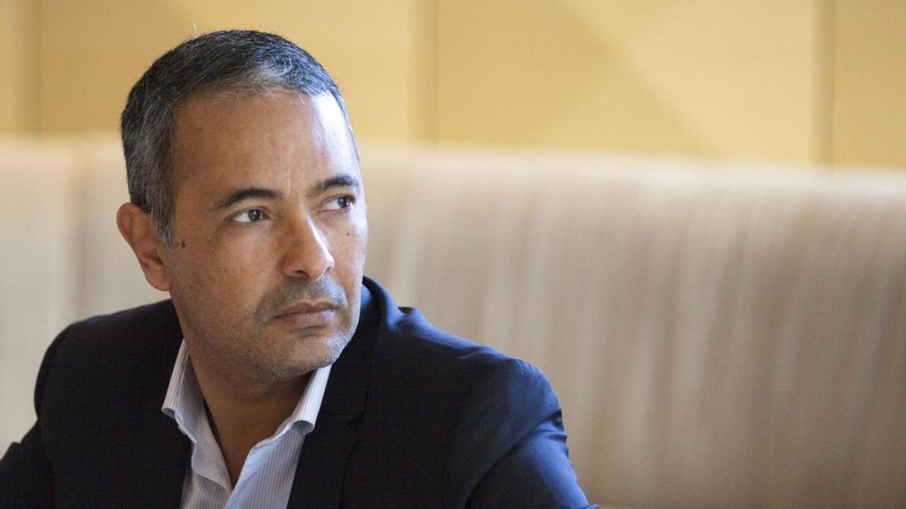 Kamel Daoud sitzt im Anzug vor edlem Ambiente. Kamel Daoud sitzt im Anzug vor edlem Ambiente.