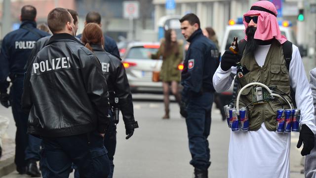 Karnevalist Sebastian (23), verkleidet als Terrorist mit "Sprengstoffgürtel" aus Energy-Drinks, steht am 15.02.2015 neben Polizisten in Braunschweig (Niedersachsen)