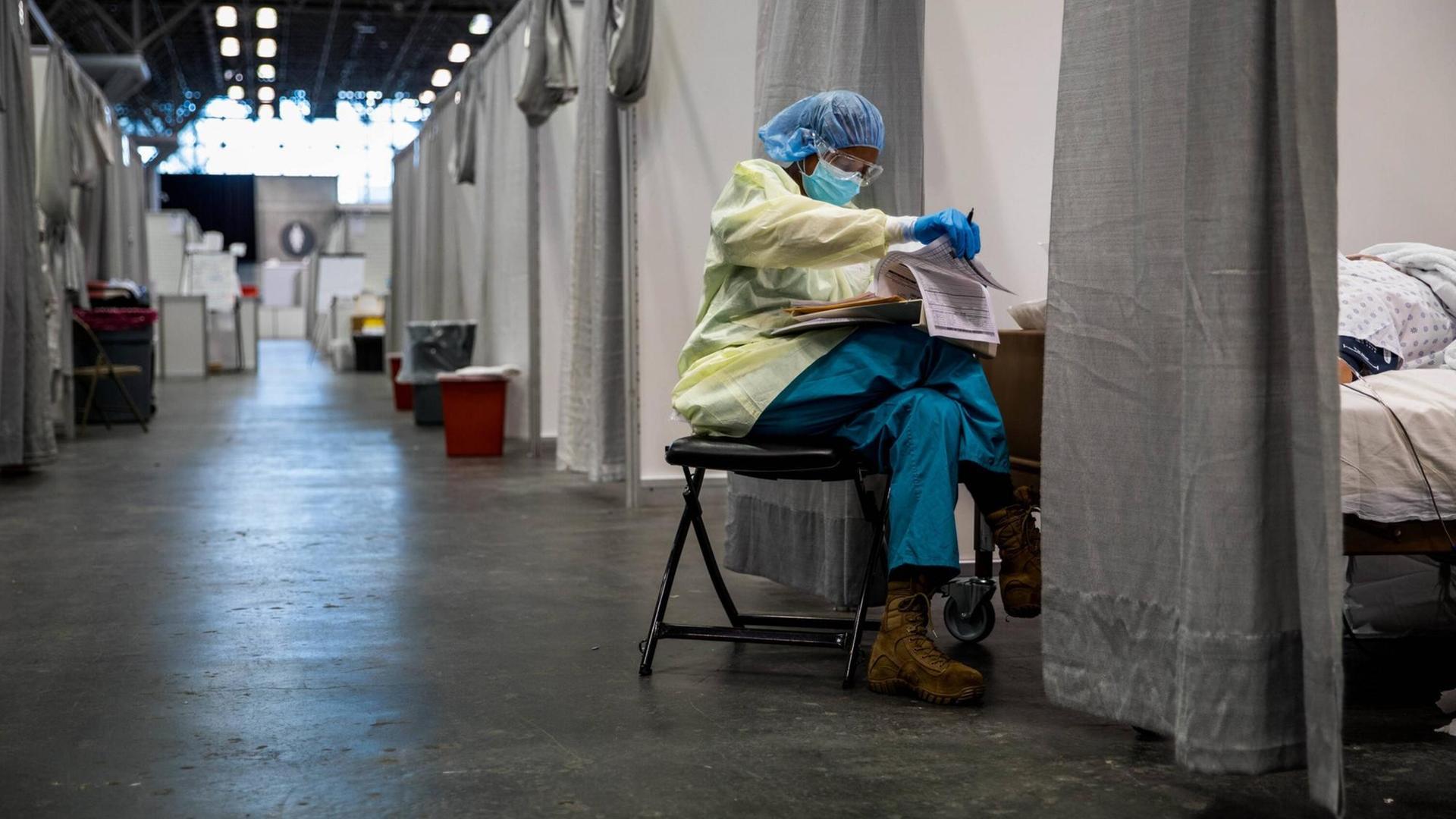 Eine medizinische Fachkraft sitzt in Schutzkleidung am Fußende einer Corona-Krankenbox in der provisorisch eingerichteten Javits New York Medical Station Eine medizinische Fachkraft sitzt in Schutzkleidung am Fußende einer Corona-Krankenbox in der provisorisch eingerichteten Javits New York Medical Station