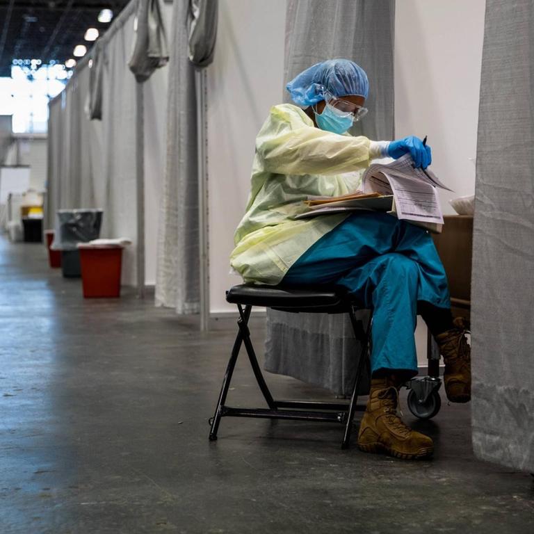 Eine medizinische Fachkraft sitzt in Schutzkleidung am Fußende einer Corona-Krankenbox in der provisorisch eingerichteten Javits New York Medical Station 