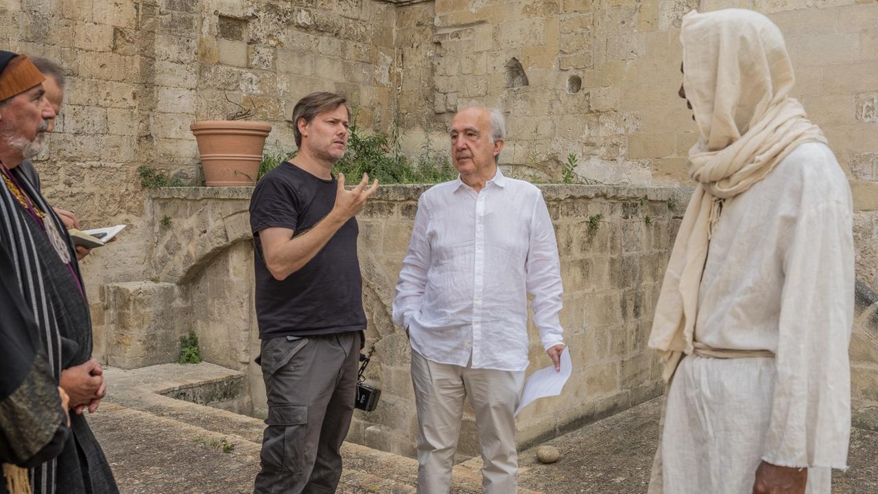 Bei den Dreharbeiten zu "Das Neue Evangelium" von Milo Rau im September 2019. Auf dem Bild ist Milo Rau im Gespräch mit Schauspielern und Mitarbeitern vor historischer Kulisse zu sehen.