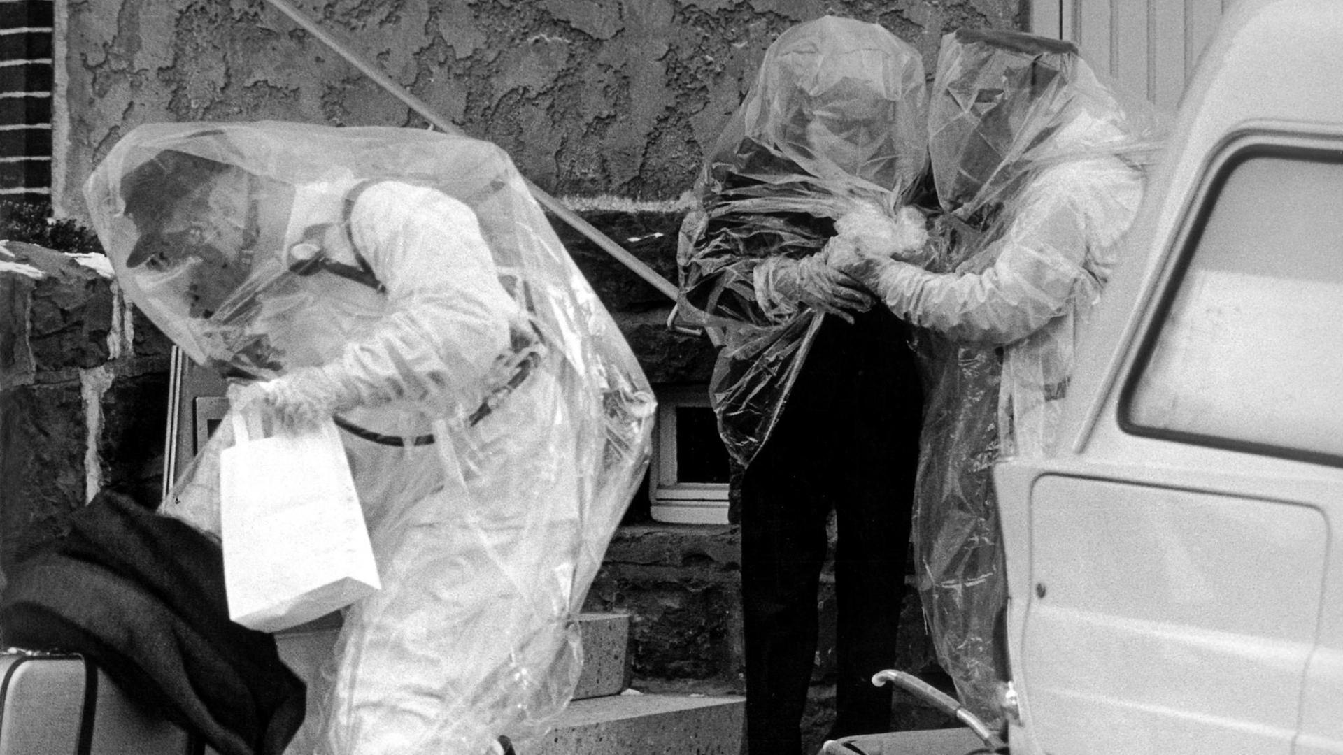 Schwarzweiß-Bild von Menschen, die sich durchsichtige Plastikumhänge über die Kleidung gezogen haben. Schwarzweiß-Bild von Menschen, die sich durchsichtige Plastikumhänge über die Kleidung gezogen haben.