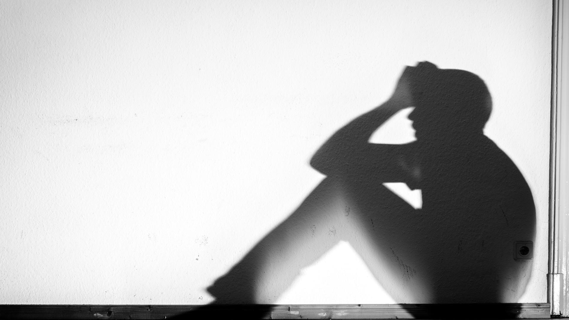 Der Schatten eines Mannes in verzweifelter Haltung wird an eine weiße Wand geworfen, aufgenommen am 01.02.2015 in Dresden (Sachsen).