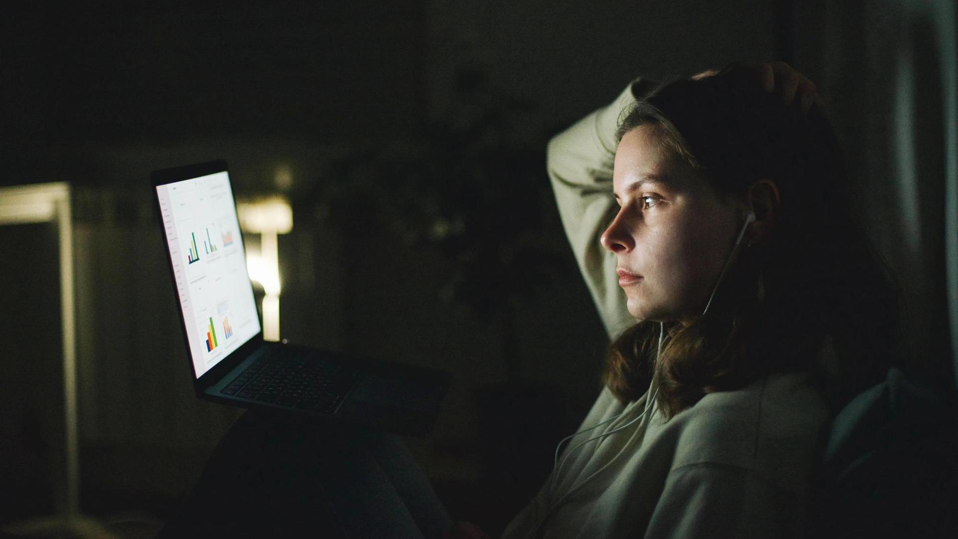 Eine Frau sitzt im Dunkeln vor einem laptop