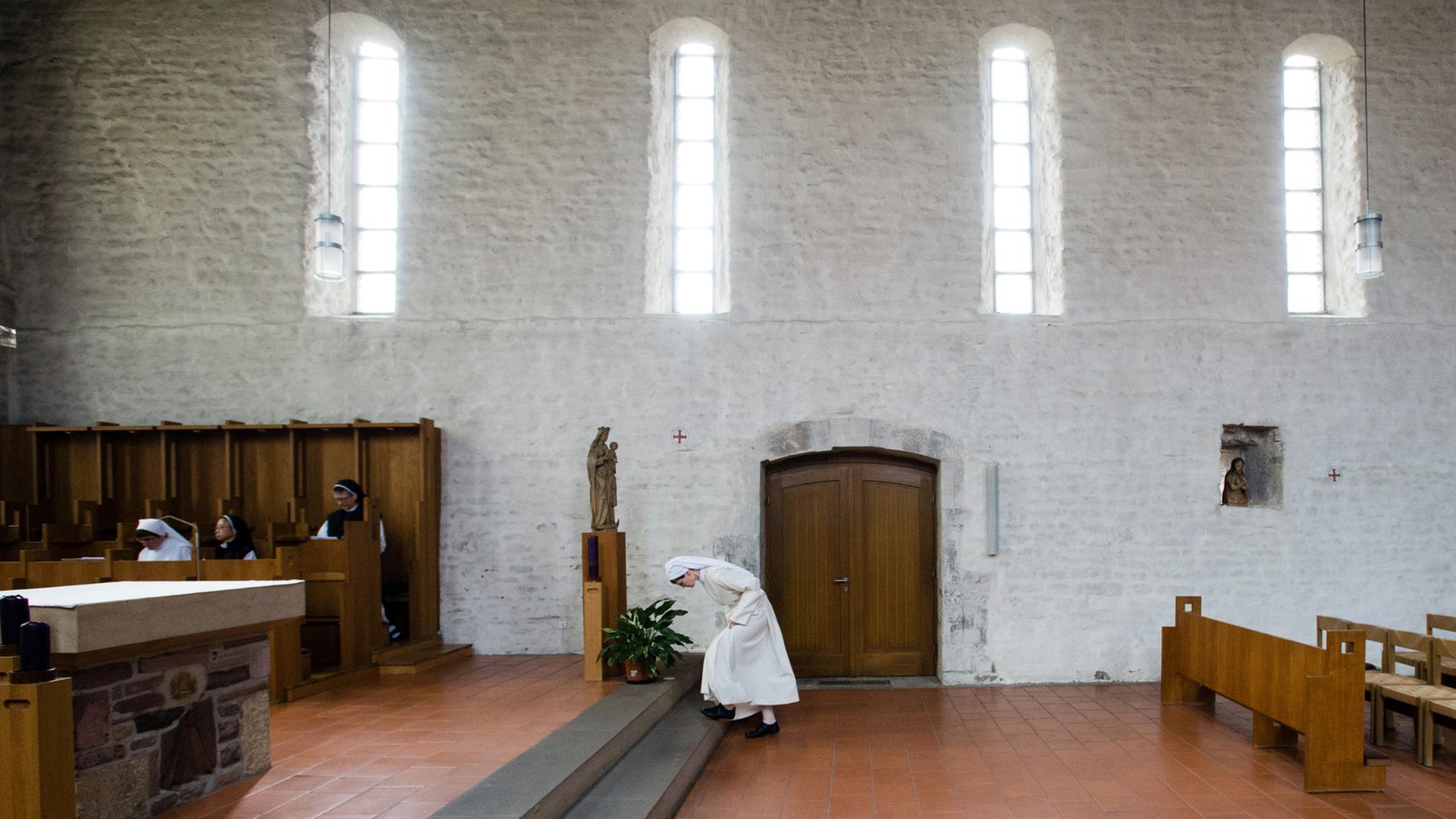 Eine Novizin verbeugt sich vor dem Altar in einer Klosterkirche.