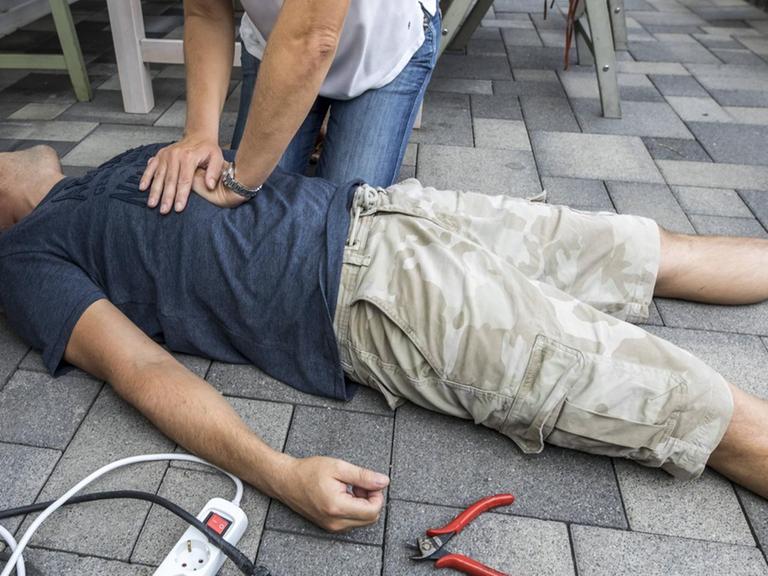 Symbolfoto: Wiederbelebung mit einer Herz-Druck-Massage nach Kreislauf- Stillstand durch Stromschlag beim Elektronik Basteln, gestellte Szene.